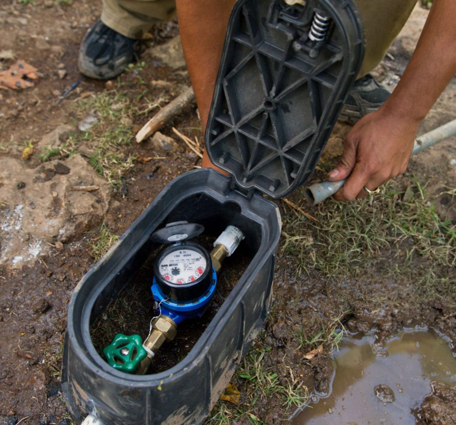 Open outdoor water meter box with standing water during a leak check.