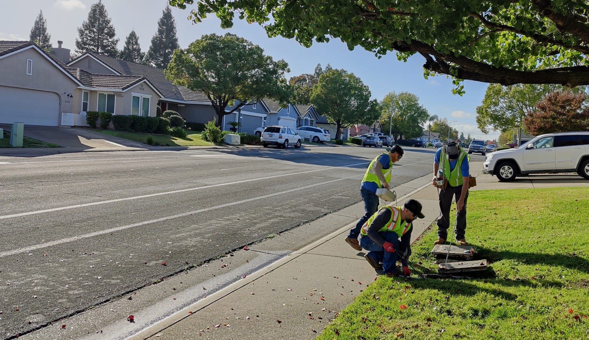 American Leak Detection technicians performing a residential street leak survey with a service van nearby.