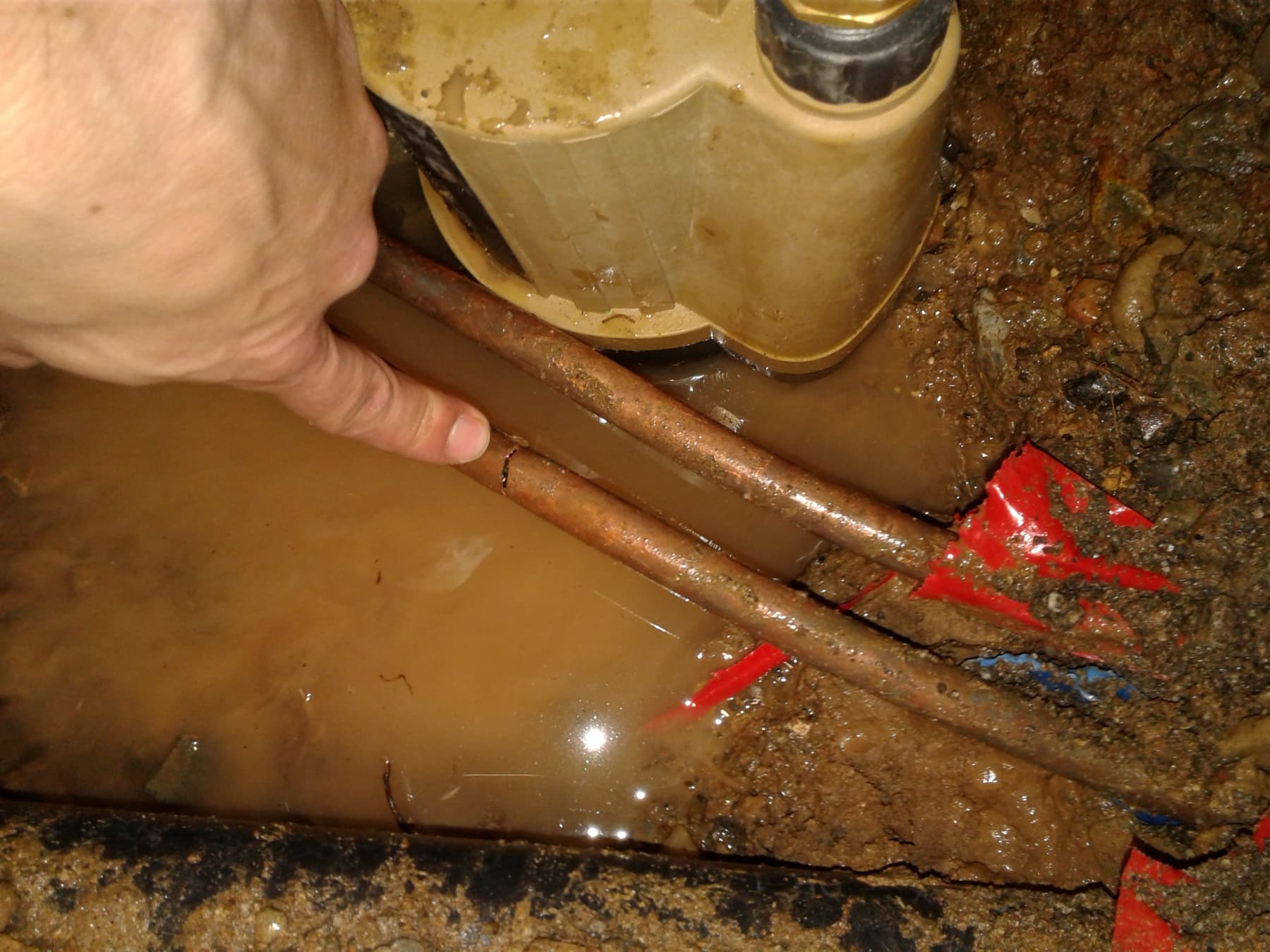 Exposed copper supply lines in standing water at a buried leak location.