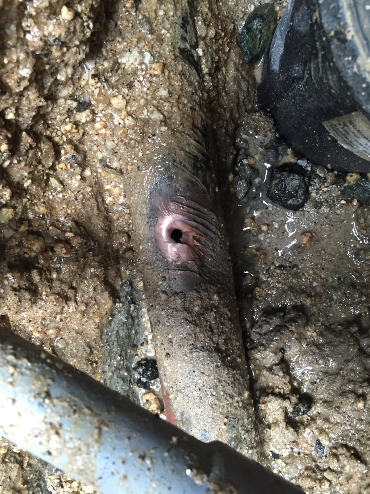 Pinhole leak in a buried supply line exposed in a wet excavation.
