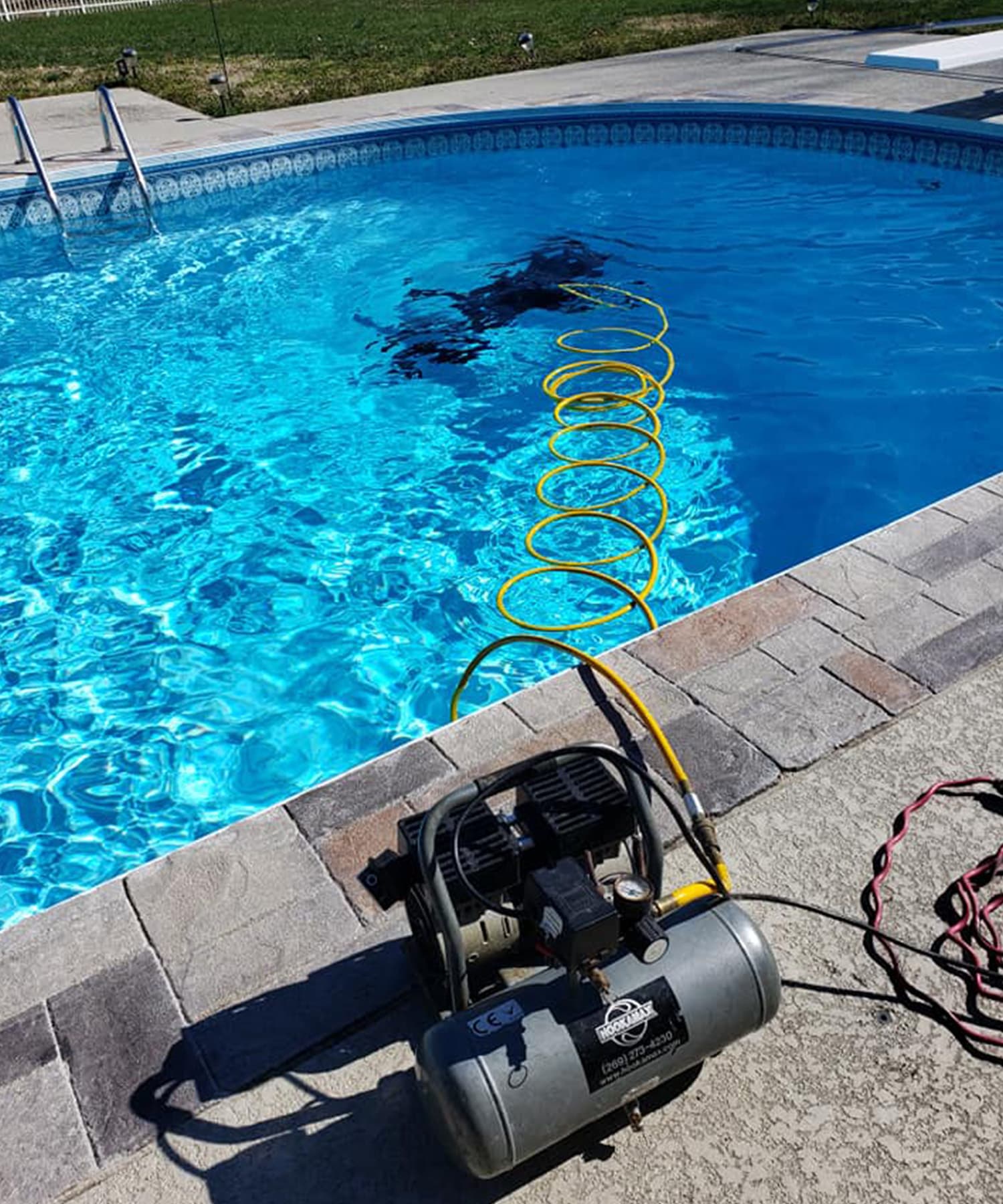 Diver inspecting a residential pool on surface-supplied air, with the hookah compressor staged on the deck.