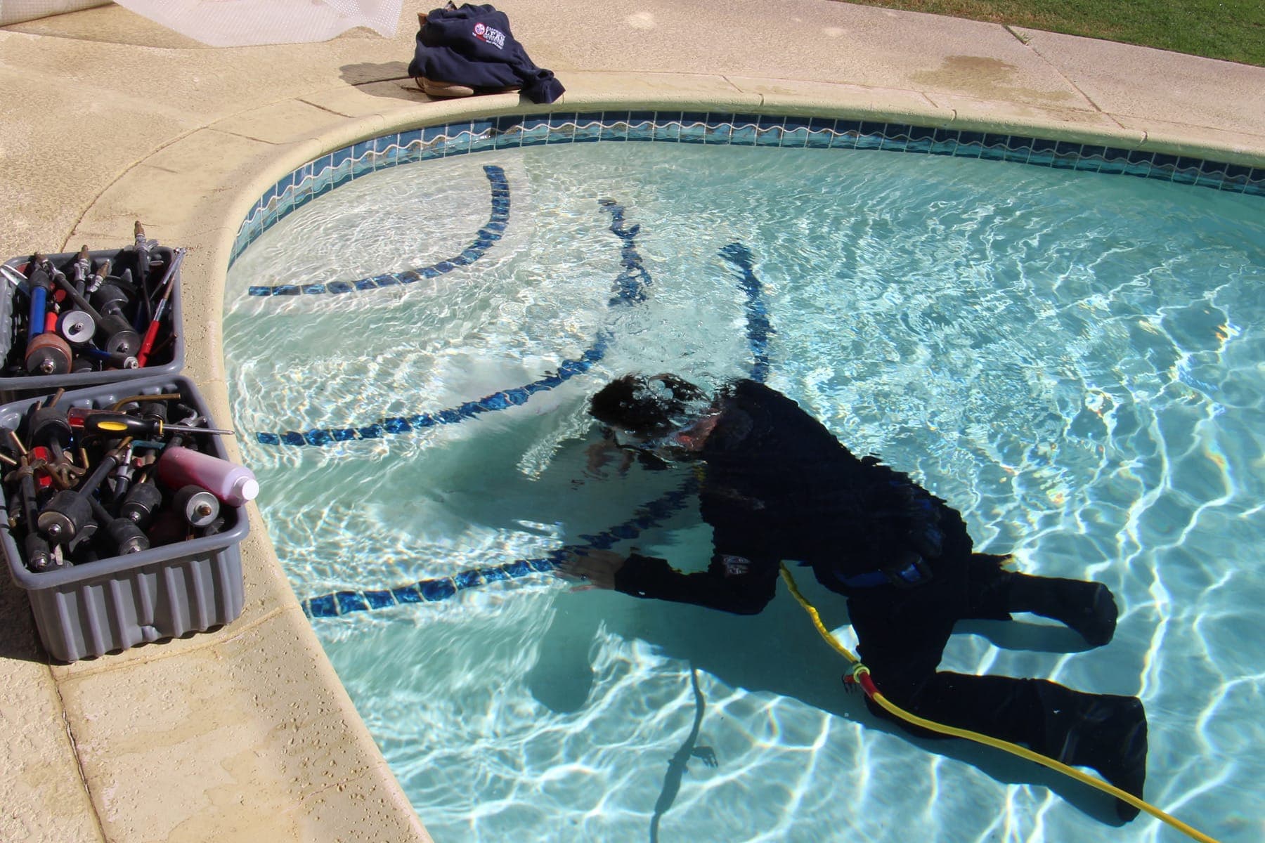 Pool diver inspecting a residential pool shell with diagnostic tools nearby.
