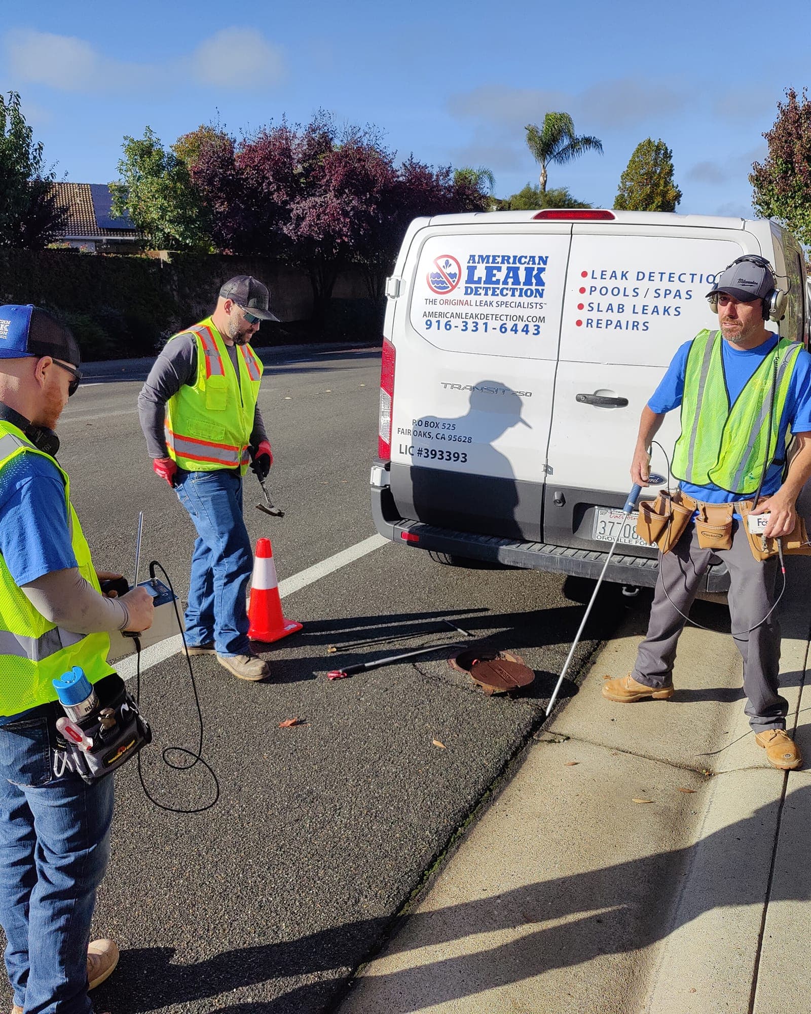 American Leak Detection crew using acoustic leak detection equipment during a curbside survey beside a service van.