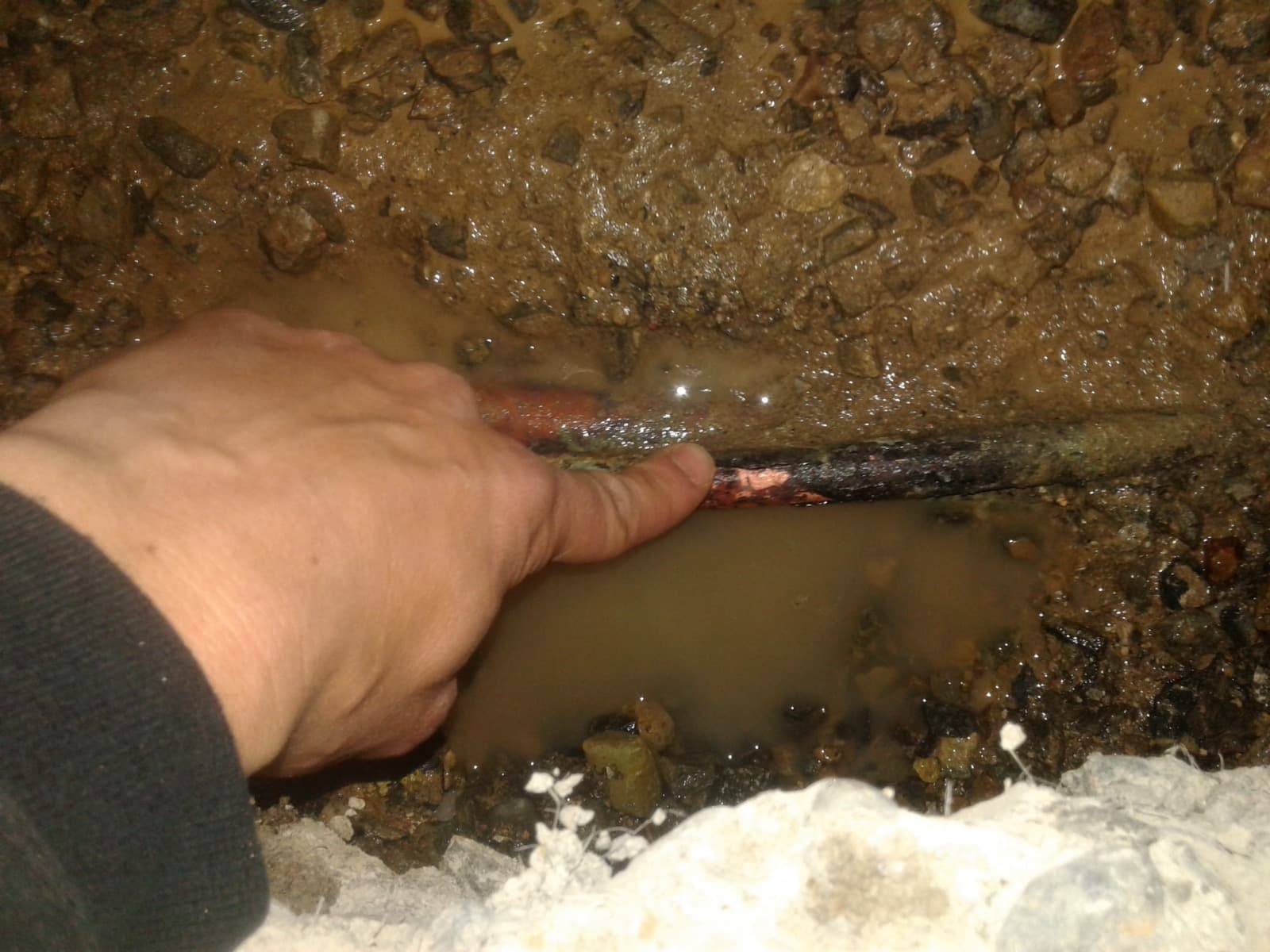 A corroded copper hot-water line exposed beneath a slab, leaking into the surrounding gravel and soil.