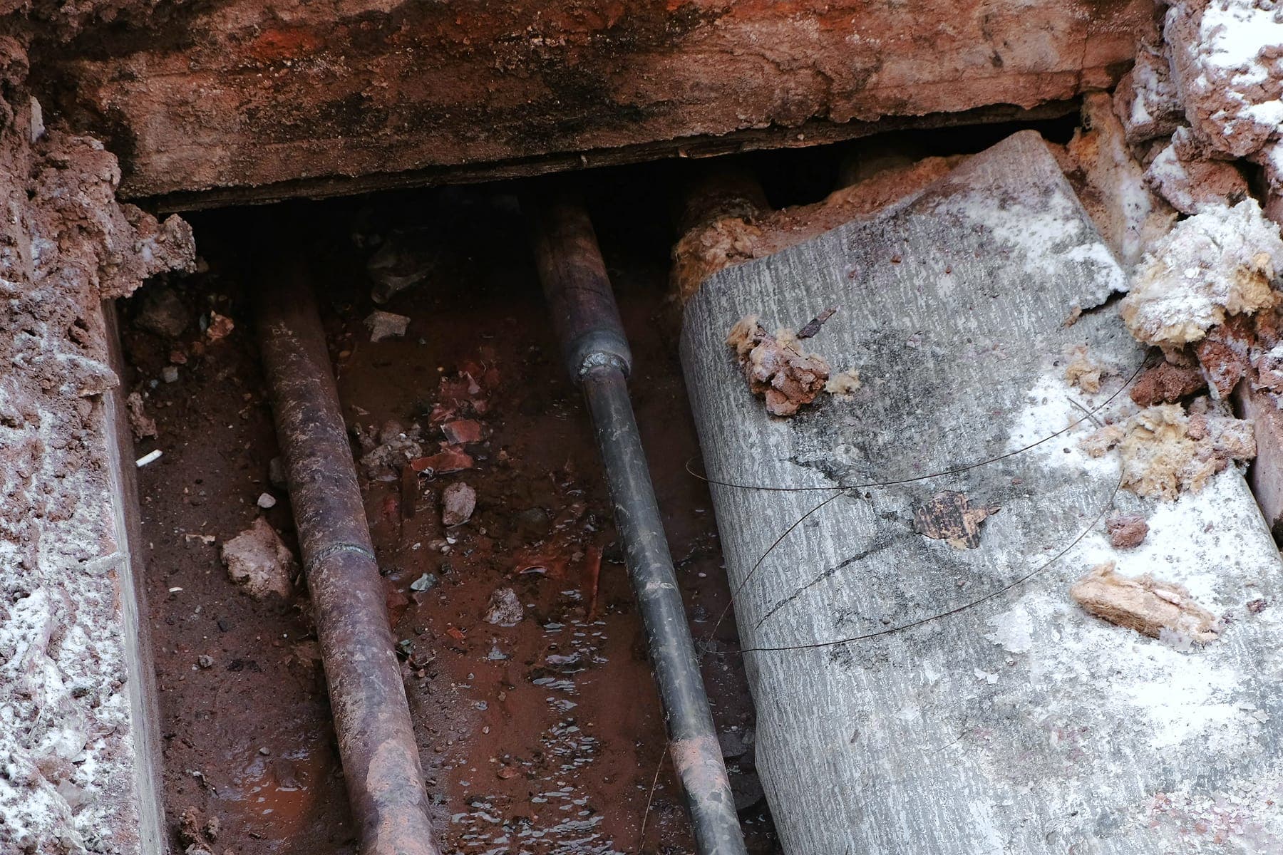 Exposed pipes below opened concrete during a slab leak investigation.