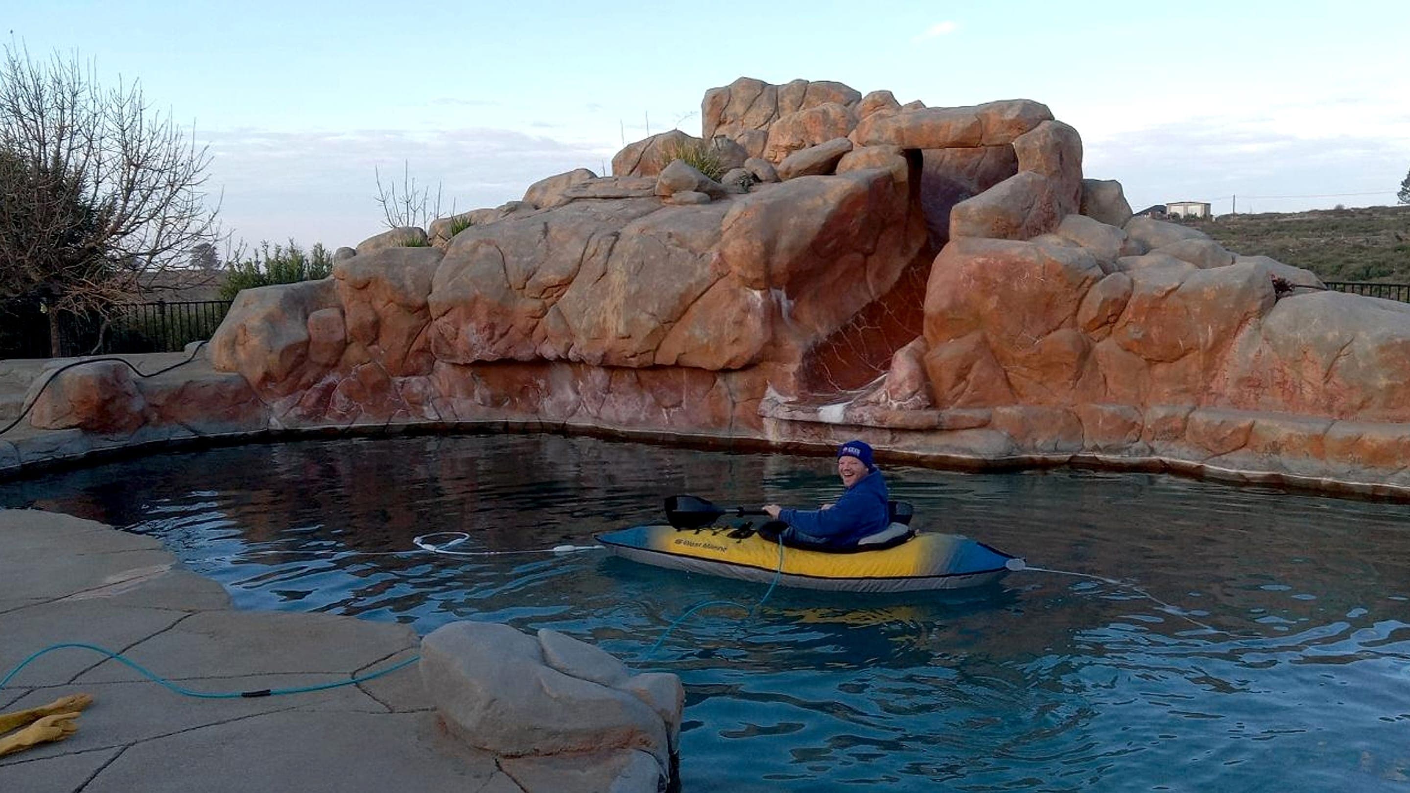 American Leak Detection specialist in a small kayak inspecting a residential pool and rock water feature for leaks.